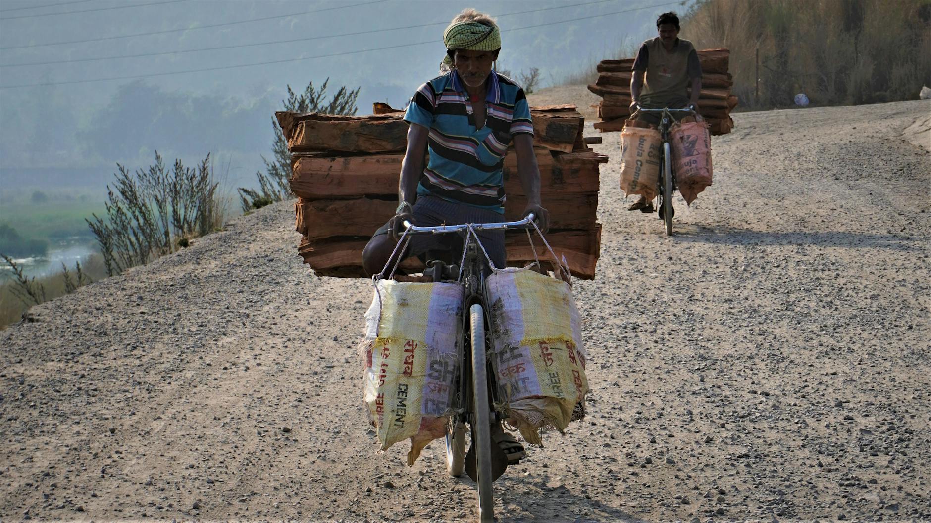 Dwaj mężczyźni na rowerach z drewnem na wiejskiej drodze w Indiach