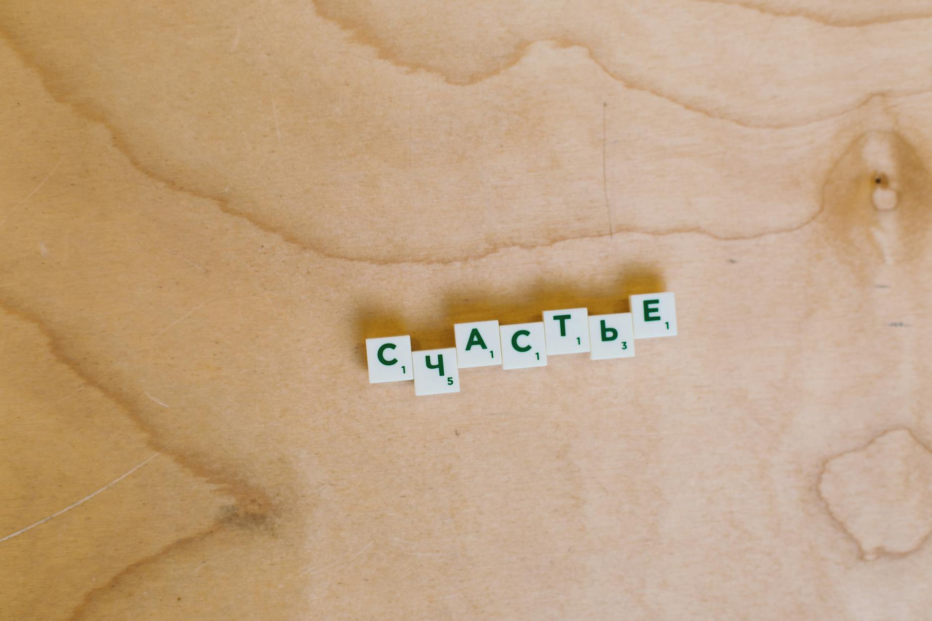 Kafelki Scrabble z rosyjskim słowem szczęście na jasnym drewnianym tle